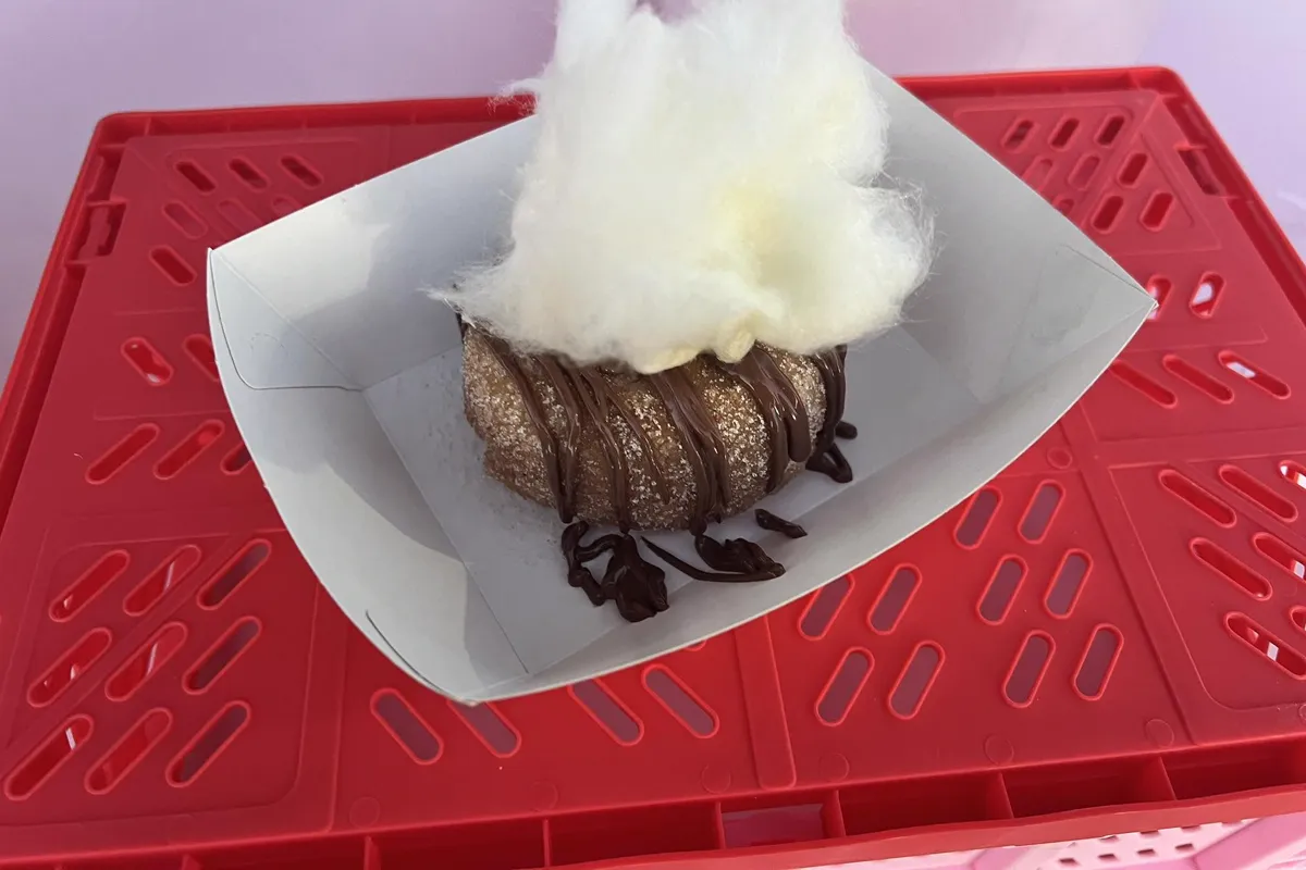 A drizzled cinnamon doughnut topped with fairy floss on a red crate