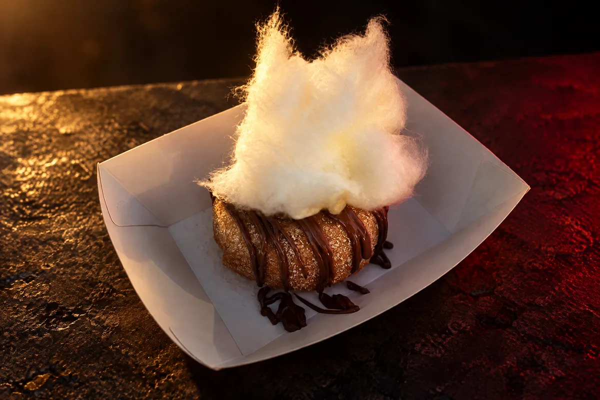 A chocolate drizzled cinnamon doughnut topped with fairy floss in warm evening light